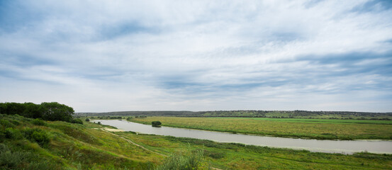 Fototapeta na wymiar Landscape river in a bright green summer field on a cloudy day