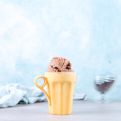 Chocolate brown ice cream in a regular yellow mug, on a blue background. Unusual serve of dessert, copy space.