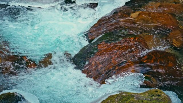 River with clear ice water with a waterfall in winter, green moss on the rocks