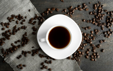 Coffee cup with roasted coffee beans on wooden table background. Mug of black coffe with scattered coffee beans on a wooden table. Fresh coffee beans.