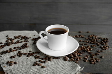 Coffee cup with roasted coffee beans on wooden table background. Mug of black coffe with scattered coffee beans on a wooden table. Fresh coffee beans.