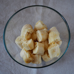 transparent glass round bowl with many slices of banana on a beige tablecloth top view.  Ingredients before baking at home