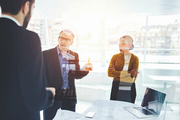 Experienced male entrepreneur analyzing financial report of economists via laptop computer connected to wifi correcting mistakes in accountings during informal meeting with employees in cabinet