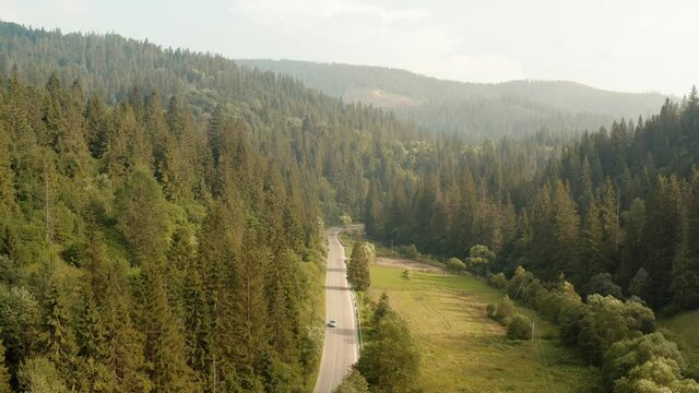 Car moving on road among green nature in the valley of mountains. Beautiful summer sunny day. Theme of travel. Aerial drone view, crane shot