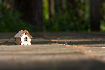 A wooden toy house in the woods, with a blurry background, stands on a wooden table. The concept of selling, buying, renting real estate, family home, home for children, insurance,  love in the house,