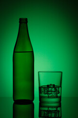 beautiful bottle with water and glass with ice and water on a green background