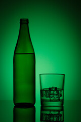beautiful bottle with water and glass with ice and water on a green background