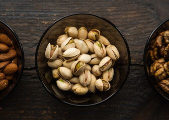 Almond, pistachio and walnut in a small plates which standing on a black table. Nuts is a healthy vegetarian protein and nutritious food.
