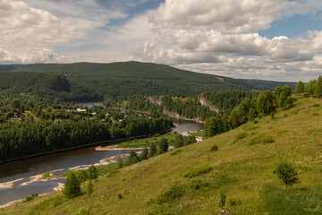 A large field next to a winding river on the background of small mountains.