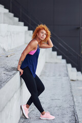 Young european redhead woman in sportive clothes standing on stairs outdoors