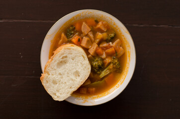 Tomato, red pepper, basil soup in white bowl with bread and spoon on a light gray background.