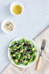 Healthy vegan salad of avocado, beetroot, greens and sesame in a white bowl. Top view, copy space