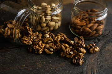 Walnut scattered on the wooden vintage table from a jar. Walnut is a healthy vegetarian protein nutritious food. Walnut kernels and whole walnuts on rustic old wood.