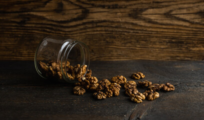 Obraz na płótnie Canvas Walnut scattered on the wooden vintage table from a jar. Walnut is a healthy vegetarian protein nutritious food. Walnut kernels and whole walnuts on rustic old wood.