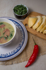 Caldo Verde Soup is a popular soup in Portuguese cuisine with greens and chopped chorizo on the top in ceramic bowl and piece of bread and pepper. Top View.