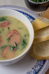 Caldo Verde Soup is a popular soup in Portuguese cuisine with greens and chopped chorizo on the top in ceramic bowl and piece of bread and pepper. Top View.
