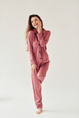 Cheerful young woman in pajamas standing indoors against white background in the studio