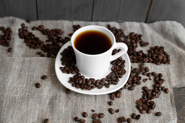Coffee cup with roasted coffee beans on linen background. Mug of black coffe with scattered coffee beans. Fresh coffee beans.