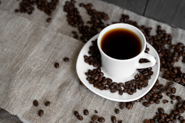 Coffee cup with roasted coffee beans on linen background. Mug of black coffe with scattered coffee beans. Fresh coffee beans.