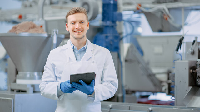 Young Male Quality Supervisor or Food Technician is Inspecting the Automated Production at a Dumpling Food Factory. Employee Uses a Tablet Computer for Work. He Looks to the Camera and Smiles.