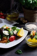 Salad in focus on white plate, with salmon and vegetables on dark wooden table, vertical image closeup