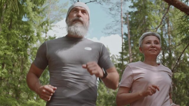 Low angle view of sporty senior man and woman wearing sportswear are running in woods in the afternoon