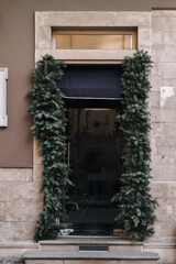 The transparent glass door with a black canopy is decorated with Christmas fir branches. The concept of the festive decor of the Krflts in the exterior.