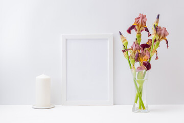 Home interior with decor elements. Mockup with a white frame and bouquet of irises flowers in a glass vase on a light background