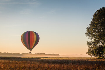 Hot Air Balloon floats over fog filled farm field and rolling hills at sunrise