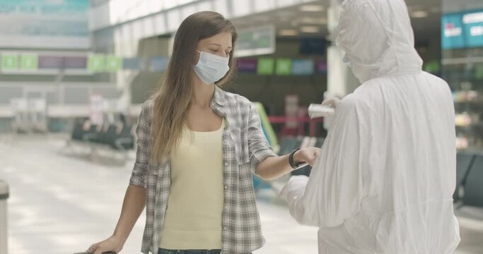Airport employee measuring temperature on hand of brunette Caucasian woman in face mask. Tourist passing scanning in departure area on Covid-19 pandemic. Coronavirus tourism. Cinema 4k ProRes HQ.