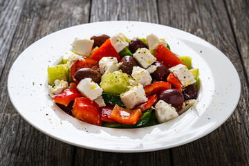 Fresh Greek salad - feta cheese, cherry tomatoes, lettuce, black olives and onion on wooden table