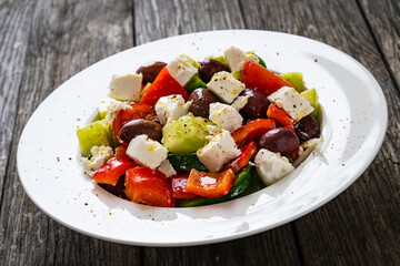 Fresh Greek salad - feta cheese, cherry tomatoes, lettuce, black olives and onion on wooden table