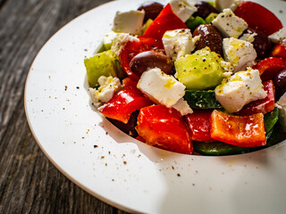 Fresh Greek salad - feta cheese, cherry tomatoes, lettuce, black olives and onion on wooden table