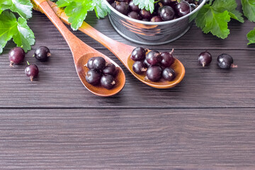 red gooseberries in a bowl and wooden spoons on the table close-up. background with red gooseberries and green leaves. gooseberries on the table
