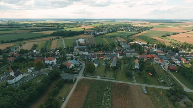 4K aerial video with the drone of a small village on the countryside while the image zooms out under cloudy weather surrounded by the wide fields of the farmers