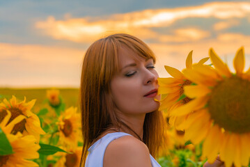 Portrait of young redhead girl in sunflower field on sunset.