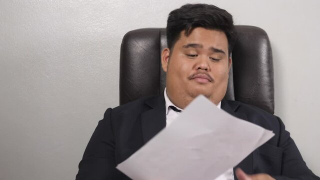 A funny Asian fat businessman wearing a suit look like the head of corporate executive or business manager receive documents for consideration for a moment causing him to be extremely dissatisfied.