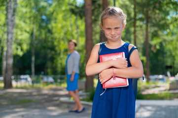 Unhappy girl with a book does not want to go to school. Mother sends daughter to first grade. The first day in elementary school.