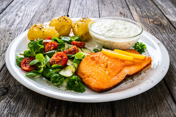 Fried salmon steak with potatoes and vegetables served on black plate on wooden table