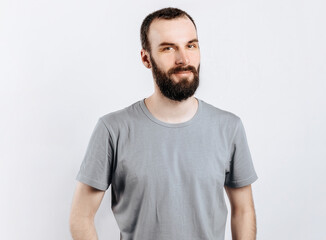 A handsome brutal brunette man with a beard in a gray shirt smiles and looks at the camera. Place for advertising on a gray background.