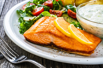 Fried salmon steak with potatoes and vegetables served on black plate on wooden table