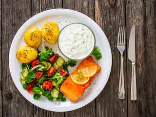 Fried salmon steak with potatoes and vegetables served on black plate on wooden table