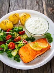 Fried salmon steak with potatoes and vegetables served on black plate on wooden table