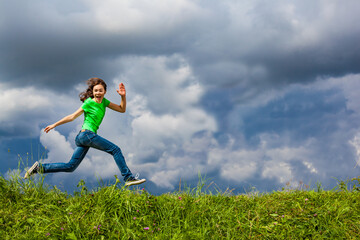 Girl jumping, running against cloudy sky

