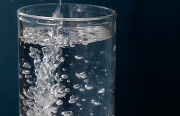 Naklejka na ściany i meble Pouring water into a glass on a dark blue background