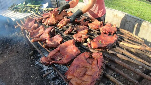 turning several pieces of suckling pig smoking on a grill