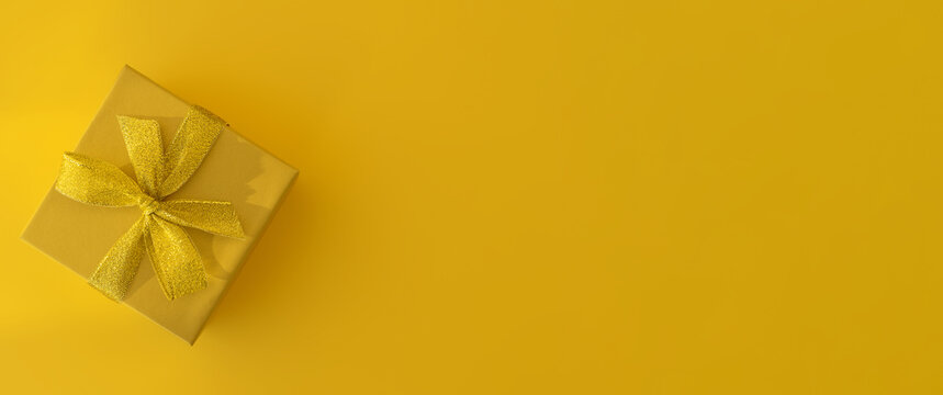 Yellow gift box with a gold bow on a yellow background. Gift for birthday, Christmas, mother's Day, Valentine's Day. Banner. Top view, horizontal position, copy space