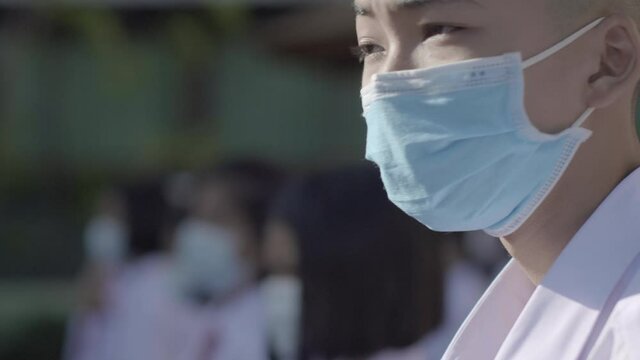 Slow motion of Asian male high school student in white uniform on the semester start wearing masks and stand in line during the Coronavirus 2019 (Covid-19) epidemic.