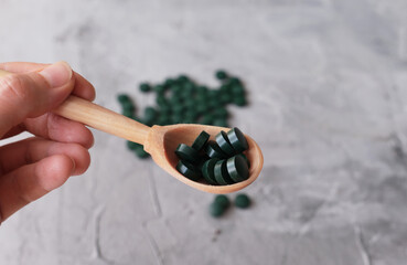 Hand of young man holding wooden spoon with chlorella tablets. Chlorella is a single-celled green algae, it is used to make nutritional supplements and medicine. Side view, copy space.