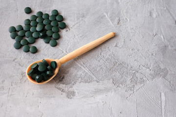 Wooden spoon with green chlorella tablets on gray concrete background. Chlorella is a single-celled green algae, it is used to make nutritional supplements and medicine. Top view, copy space.